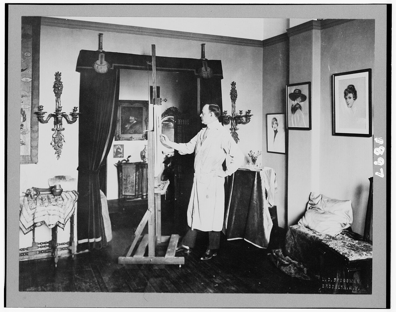 Illustrator Hamilton King standing at his easel, photographed in the early 1900s